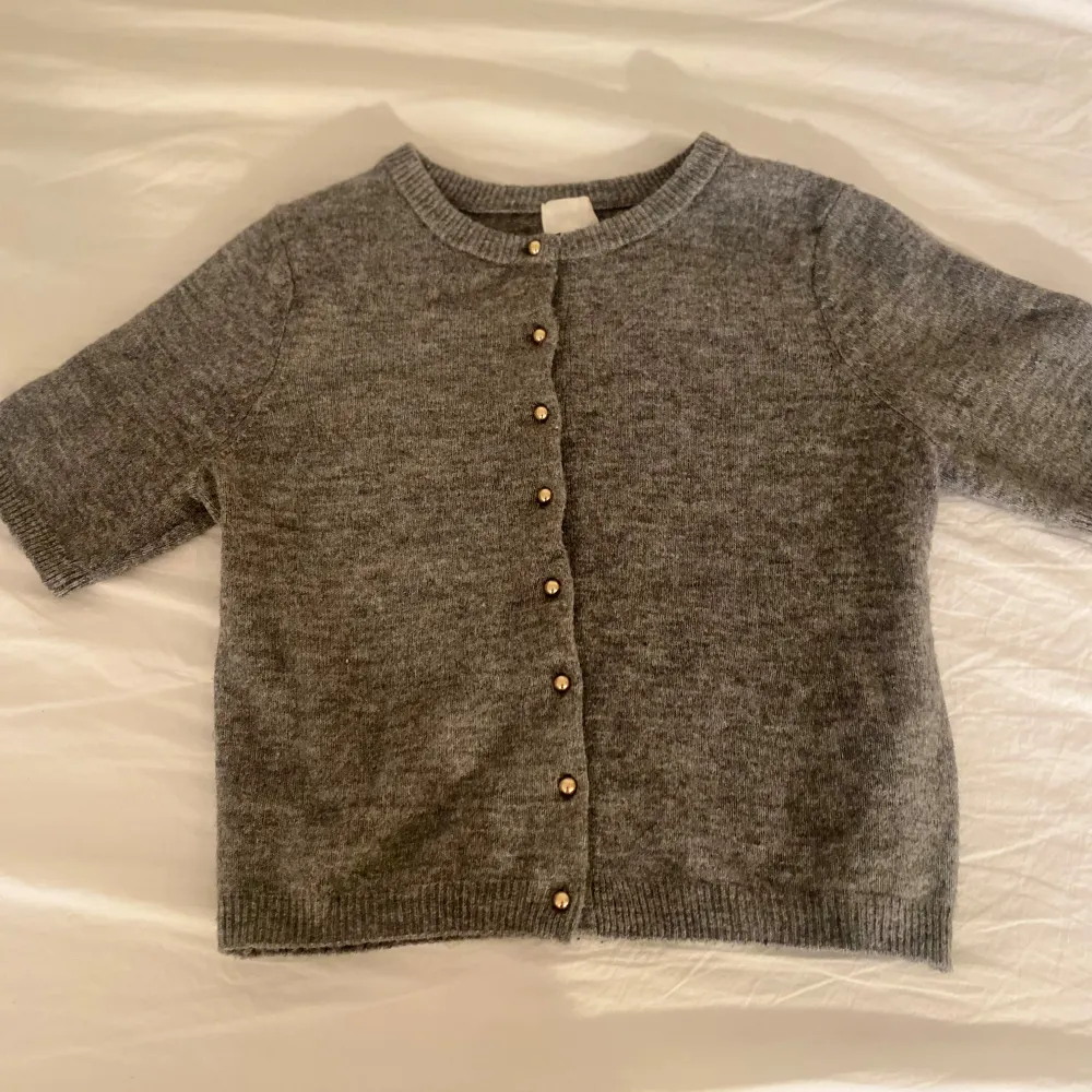 Säljer en stilren grå kofta med korta ärmar och knappar framtill. Den passar till många olika outfits. Ett måste i garderoben för den som gillar klassiska plagg.. Neuletakit & Villapaidat.