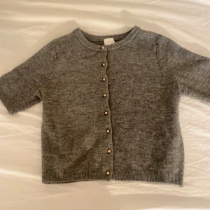 Grå kofta med knappar - Säljer en stilren grå kofta med korta ärmar och knappar framtill. Den passar till många olika outfits. Ett måste i garderoben för den som gillar klassiska plagg.