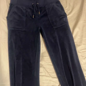 Mörkblå juicy byxor med fickor - Säljer ett par mörkblå juicy  byxor med bred resår och snörning i midjan. Byxorna har praktiska fickor både fram och bak med knappdetaljer. Perfekta för en avslappnad stil. Säljer dom då jag inte får dom till nytta längre 