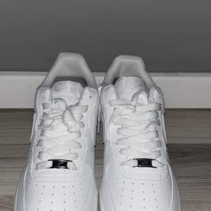 Vita Nike Air Force sneakers - Säljer ett par klassiska vita Nike Air Force sneakers. Skorna har en stilren design med snörning och Nike-logga på sidan och hälen. Perfekta för en clean look.