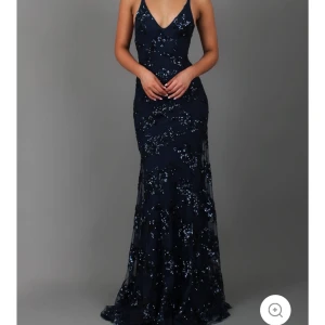 Mörkblå balklänning - Fin mörkblå klänning med glittrande paljetter och v-ringad design. Klänningen har en öppen rygg med snörning och smala axelband. Perfekt för balen. För kort för mig som är 173cm, Köpt på jardins vue. Helt ny!!
