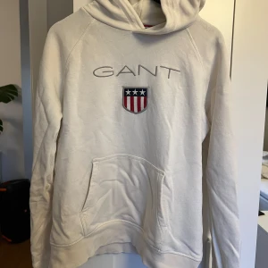 Vit hoodie från GANT - Välanvänd Gant hoodie. Den har en liten fläck på luvan (se bild) och loggan är även lite sliten fram till. Men annars i fint skick. Den är skrynklig för att den har legat längst in i min garderob ett tag.💙🤍