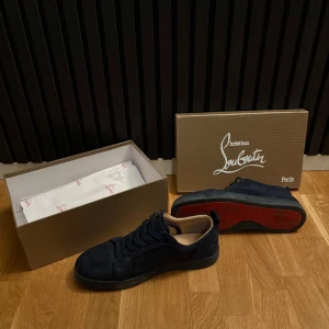 Loubs - Snygga mörkblå sneakers från Christian Louboutin med den ikoniska röda sulan. Skorna har en stilren design med snörning och är tillverkade i mocka. Perfekta för den som vill ha en touch av lyx i vardagen. Skick 8/10 då tecken på användning finns! 😀 