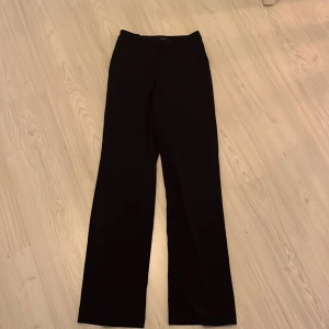 Svarta kostymbyxor från Vero Moda - Snygga svarta kostymbyxor från Vero Moda med rak passform. Perfekta för en stilren look. Byxorna har en klassisk design med dragkedja och knapp framtill.