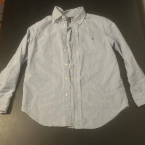 Ljusblå skjorta från Ralph Lauren - Säljer en stilren ljusblå skjorta från Ralph Lauren, perfekt till sommaren! Strl 14 år-Kan funka som XXS/XS