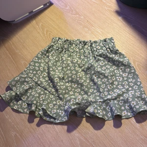 Gröna blommiga kjol med volang - Säljer en söt kjol med vita blommor och volangdetaljer. Perfekta för sommardagar! 🌼