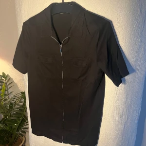 Kortärmad skjorta med dragkedja - Kortärmad svart skjorta med dragkedja från märket ”Cappuccini”. Kika gärna andra annonser också, samfrakta gärna.