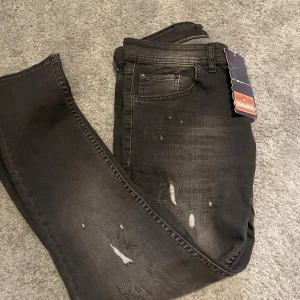 Svarta jeans  - Snygga svarta jeans från Dsquared  med slitna detaljer för en trendig look. Jeansen har en klassisk femficksdesign och en bekväm passform. Perfekta för att ge din outfit en edgy touch. Storlek 32 32 men passar mycket mindre, passar mig perfekt som är 179