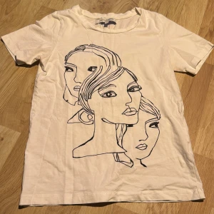 Vit t-shirt med ansiktsmotiv från KappAhl - Säljer en vit t-shirt från KappAhl med ett ansiktsmotiv i svart på framsidan. T-shirten är kortärmad och gjord i mjuk bomull. Strl Xs