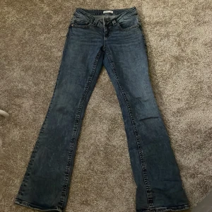 Blå jeans från Gina tricot  - Snygga blå jeans från Gina tricot med klassisk femficksdesign och knappgylf. De har en bootcut-stil som ger en retro känsla. Perfekta för en avslappnad look. 
