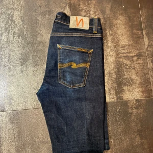 Mörkblå jeans från Nudie Jeans - Snygga mörkblå jeans från Nudie Jeans med klassisk femficksdesign och kontrastsömmar. Jeansen har en smal passform och är tillverkade i högkvalitativt denim. Perfekta för en stilren look.