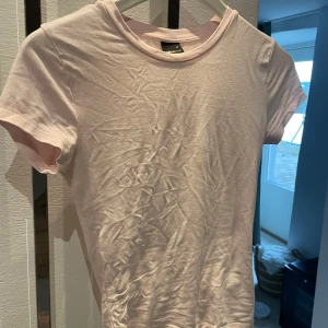 Ljusrosa t-shirt från Gina Tricot - Säljer en söt ljusrosa t-shirt från Gina Tricot. Den är kortärmad och gjord i mjuk bomull, perfekt för en avslappnad stil. Soft touch kollektionen.