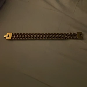 Guldarmband från Edblad - Elegant guldarmband med en bred flätad design och ett stilrent lås. Perfekt för att ge en touch av lyx till din outfit.