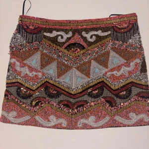 Ibiza-stil Kjol -  Den här kjolen är ett riktigt statement-piece! Täckt av handsydda paljetter och pärlor som gnistrar i varje rörelse. Tung och lyxig kvalitet som ger en exklusiv känsla.  Nyskick, använd få gånger. Extra påse med pärlor medföljer. Storlek XS  Nypris ca 3000 kr – nu din chans att glänsa!