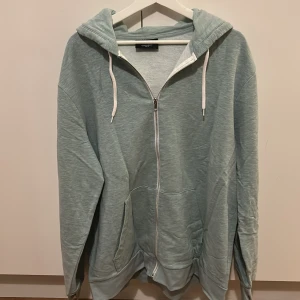 Ljusblå huvtröja från H&M - Säljer en ljusblå huvtröja från H&M med dragkedja och fickor framtill. Tröjan har en bekväm passform och är perfekt för avslappnade dagar. Den har långa ärmar och en justerbar huva med snören.