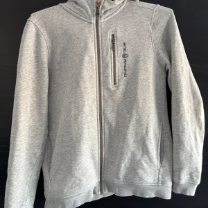 Grå hoodie från Sail Racing - Hej, säljer en hoodie från Sail Racing i storlek 160. Tröjan är i bra skick förutom att det finns slitage på båda armarna vid handled men också vid armbåge där av det låga priset. Jag kan gå ner i pris vid snabb affär. Mvh