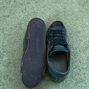 Gröna sneakers från Philippe Model(storlek 43) - Snygga gröna sneakers från Philippe Model med svarta snören och detaljer. Skorna har en robust sula och är perfekta för en stilren look. Tillverkade i Italien.