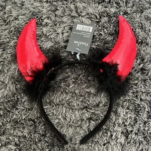 Rött diadem med horn och fjädrar - Snyggt diadem med röda horn och svarta fjädrar, perfekt för en festlig look. Hornens material ger en glansig finish och fjädrarna tillför en extra touch av dramatik.