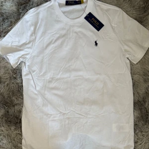 Vit och svart t-shirt från Polo Ralph Lauren - Säljer två klassiska t-shirts från Polo Ralph Lauren i vit och svart. Båda har korta ärmar och den ikoniska broderade loggan på bröstet. Perfekta för en stilren look.