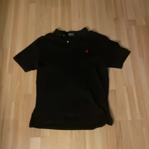 Svart pikétröja från Ralph Lauren - Klassisk svart pikétröja från Ralph Lauren med röd broderad logga på bröstet😁 Tröjan har korta ärmar och knappar vid kragen och är perfekt nu för sommarn eller nu på hösten ✔️⛱️🍁(Priset för att diskuteras vid snabbt köp)
