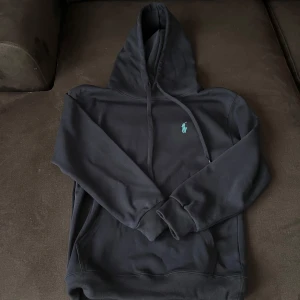 Polo ralph lauren hoodie - Säljer en stilren mörkblå hoodie från Ralph Lauren med det klassiska logotypen broderad i blått på bröstet. Tröjan har en bekväm passform med långa ärmar och en praktisk huva med dragsko. Perfekt för en avslappnad look.