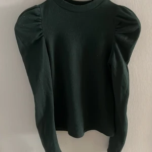 Mörkgrön långärmad topp - Snygg mörkgrön topp med långa ärmar och puffiga axlar. Perfekt för en stilren look. Tillverkad i ett mjukt material som känns skönt mot huden.