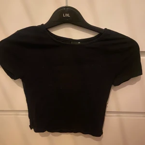 Svart croppad topp från Gina Tricot - Säljer en svart croppad topp från Gina Tricot. Toppen har korta ärmar och en enkel design som passar perfekt till olika outfits. Perfekt för en stilren look!