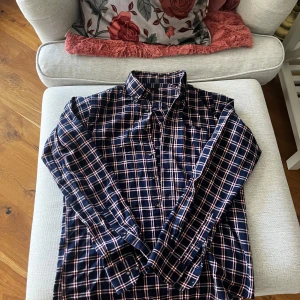 Rutig skjorta från Dressmann - Snygg rutig skjorta från Dressmann i marinblått, vitt och rött. Skjortan har långa ärmar och klassisk krage med knappar framtill. Perfekt för en stilren look.