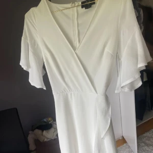 Vit omlottklänning - Säljer en elegant vit omlottklänning. Klänningen har korta ärmar och en v-ringad design som ger en stilren look. Perfekt för sommarens alla tillfällen. 🕊️