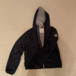 Marinblå windbreaker från Moncler - Säljer en äkta marinblå windbreaker från Moncler.  Storlek 14y, passar bäst på dig som är runt 160 -170 kan passa mindre eller större. Skicket är mycket bra, bara använd fåtalet gånger. Priset kan diskuteras vid snabb affär!