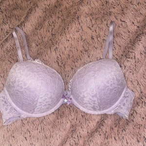 Lila pushup-bh från Hunkemöller - Säljer en vacker lila bh från Hunkemöller med spetsdetaljer och en söt rosett framtill. Säljer då den var för stor.