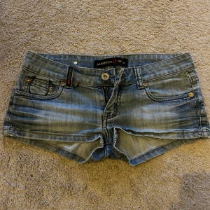 Blå jeansshorts från Musketeer Jeans - Snygga blå jeansshorts från Musketeer Jeans med coola detaljer som broderad text på baksidan och klassiska femficksdesign. Perfekta för en avslappnad stil. Storlek S/M, står inte storlek men runt däromkring 