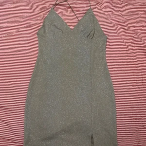 Glittrig klänning från H&M Divided - Snygg glittrig klänning från H&M Divided i en elegant beige ton. Klänningen har en v-ringad design med smala axelband som korsas i ryggen och en liten slits framtill. Perfekt för en kväll ute! ✨