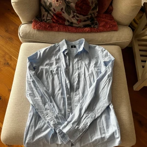 Ljusblå skjorta från Lager 157 - Säljer en stilren ljusblå skjorta från Premium Basic i storlek medium. Skjortan har långa ärmar och knappar framtill. Perfekt för en klassisk look.