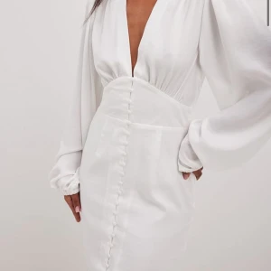 Vit klänning med v-ringning - Elegant vit klänning med djup v-ringning och långa ärmar. Klänningen har en figursydd passform med knapprad framtill som ger en stilren look. Perfekt för speciella tillfällen. Slutsåld på hemsidan nypris 699kr fler och egna bilder fås privat, perfekt till student 
