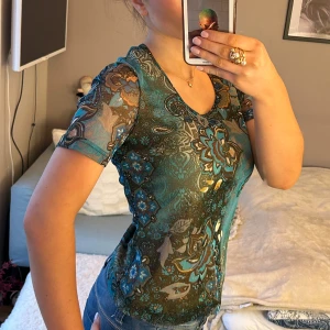 Blommig topp från Taifun - Säljer en färgglad topp från Taifun med blommigt mönster i blått och brunt. Toppen har korta ärmar och en rund halsringning. I storlek S 💐