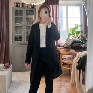 Svart kappa - Snygg svart kappa med klassisk design. Perfekt för att hålla stilen under kyligare dagar. Den har långa ärmar och en rak passform som ger en elegant look.