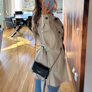 Beige kappa med knappar - Snygg beige kappa med knappar och bälte i midjan. Perfekt för höst och vår. 