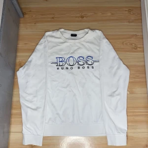 Vit tröja från Hugo Boss - Säljer en stilren vit tröja från Hugo Boss med blå och svart logga på framsidan. Tröjan har en slim fit passform och långa ärmar. Perfekt för en avslappnad men ändå snygg look.
