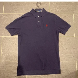 Mörkblå pikétröja från Ralph Lauren - Säljer en klassisk mörkblå pikétröja från Ralph Lauren med den ikoniska röda loggan på bröstet. Pris kan diskuteras 