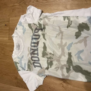 kamouflage t-shirt från Dondup - Säljer en snygg t-shirt från Dondup med kamouflagemönster i gröna och beige toner på framsidan. T-shirten är kortärmad och har en vit baksida. Perfekt för en avslappnad stil. Nypris runt 1200 kr 