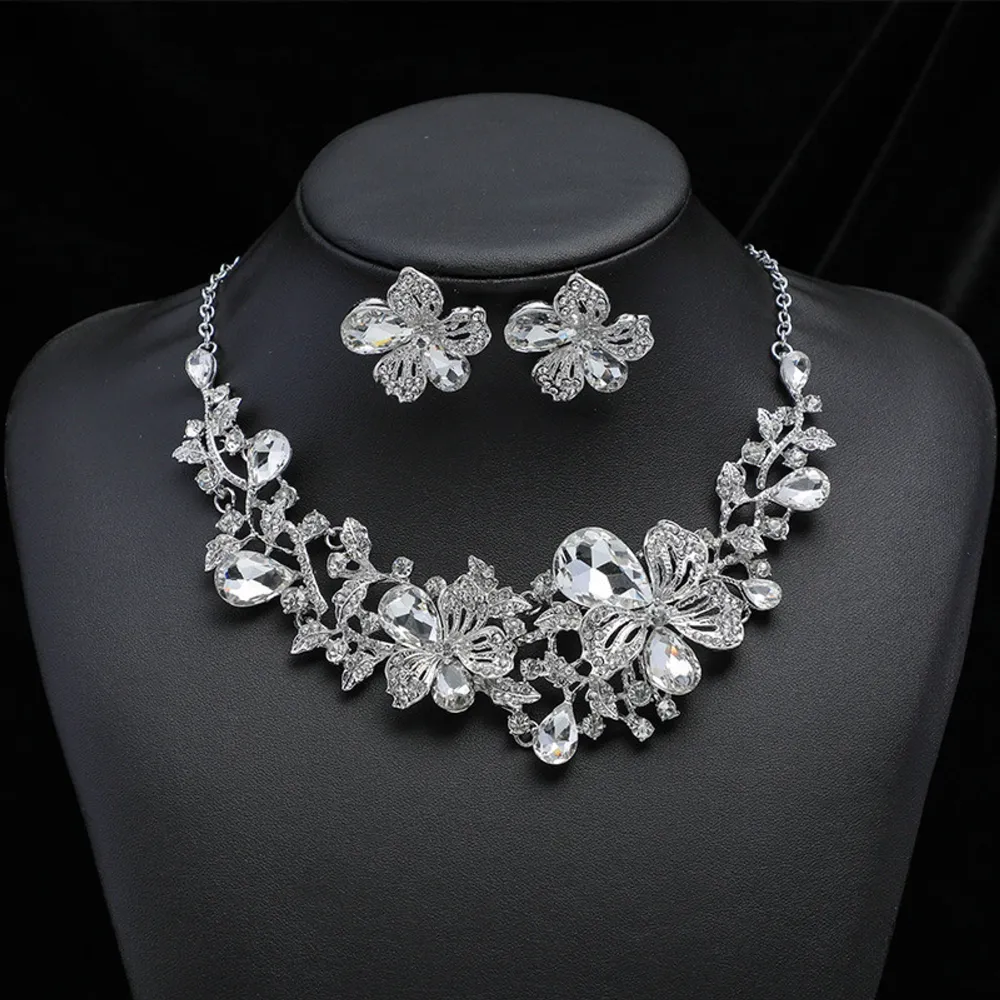 Elegant halsband och örhängen i silverfärg med blommotiv och glittrande stenar. Halsbandet har en justerbar kedja och matchande örhängen med samma blommönster. Perfekt för att ge en gnistrande touch till din outfit.. Asusteet.