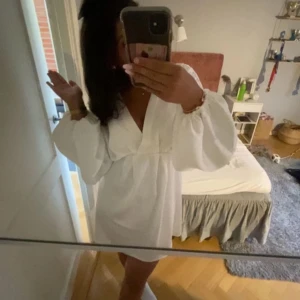 Vit klänning från Gina Tricot - Säljer en elegant vit klänning från Gina Tricot med v-ringad design och långa ärmar. Perfekt för en stilren look. Klänningen har en lös passform och är tillverkad i ett mjukt material. Funkar perfekt som studentklänning.
