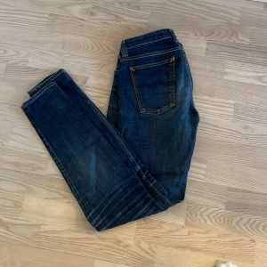 Mörkblå jean från nudie - Snygga mörkblå jeans med klassisk femficksdesign och orange sömmar. De har en dragkedja och knapp framtill. Perfekta för en avslappnad stil.
