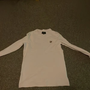 Vit långärmad tröja från Lyle & Scott - Säljer en stilren vit långärmad tröja från Lyle & Scott med deras ikoniska logga på bröstet. Perfekt för en avslappnad och snygg look. Passar bra till både jeans och chinos.