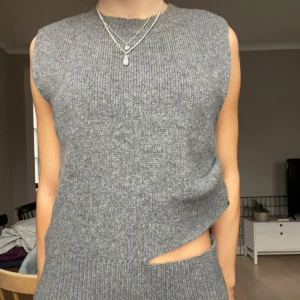 Grå stickad väst - Snygg grå stickad väst med en unik asymmetrisk design. Västen har en ribbad struktur och är ärmlös, vilket gör den perfekt för lager-på-lager-stil. Passar bra till både vardag och speciella tillfällen. Nyskick!!💘💘