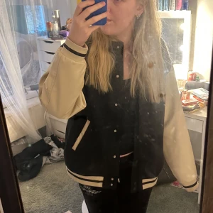 Svart och beige bomberjacka - Säljer en snygg svart och beige bomberjacka från H&M. Jackan har långa ärmar och stängs med knappar. Den har ribbade muddar och två fickor framtill. Perfekt för en cool och avslappnad stil. Har tecken på användning såsom noppror som lätt går bort.