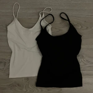 Svart och vit linnetopp från Gina Tricot - Säljer två stilrena linnetoppar från Gina Tricot i svart och vitt. Perfekta basplagg med smala axelband och en enkel design. Passar till alla tillfällen och är lätta att matcha med andra plagg. Perfekt för lager-på-lager eller som de är. Kan sänka pris vid snabbaffär!