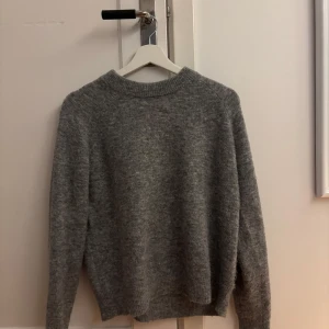 Grå stickad tröja från Zara - Mysig grå stickad tröja från Zara. Perfekt för kyliga dagar med sin mjuka och bekväma passform. Tröjan har långa ärmar och en rund halsringning. Ett stilrent val för garderoben!