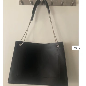 Svart axelväska från Filippa K - Snygg svart axelväska från Filippa K i skinn. Väskan har en stilren design med silverfärgade kedjehandtag och en diskret logotyp på insidan. Perfekt för att bära dina dagliga nödvändigheter med stil.